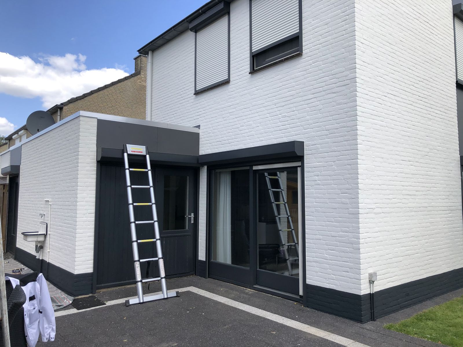 Rijtjeshuis met wit geschilderde gevel, antraciet kozijnen en twee ladders tegen de gevel