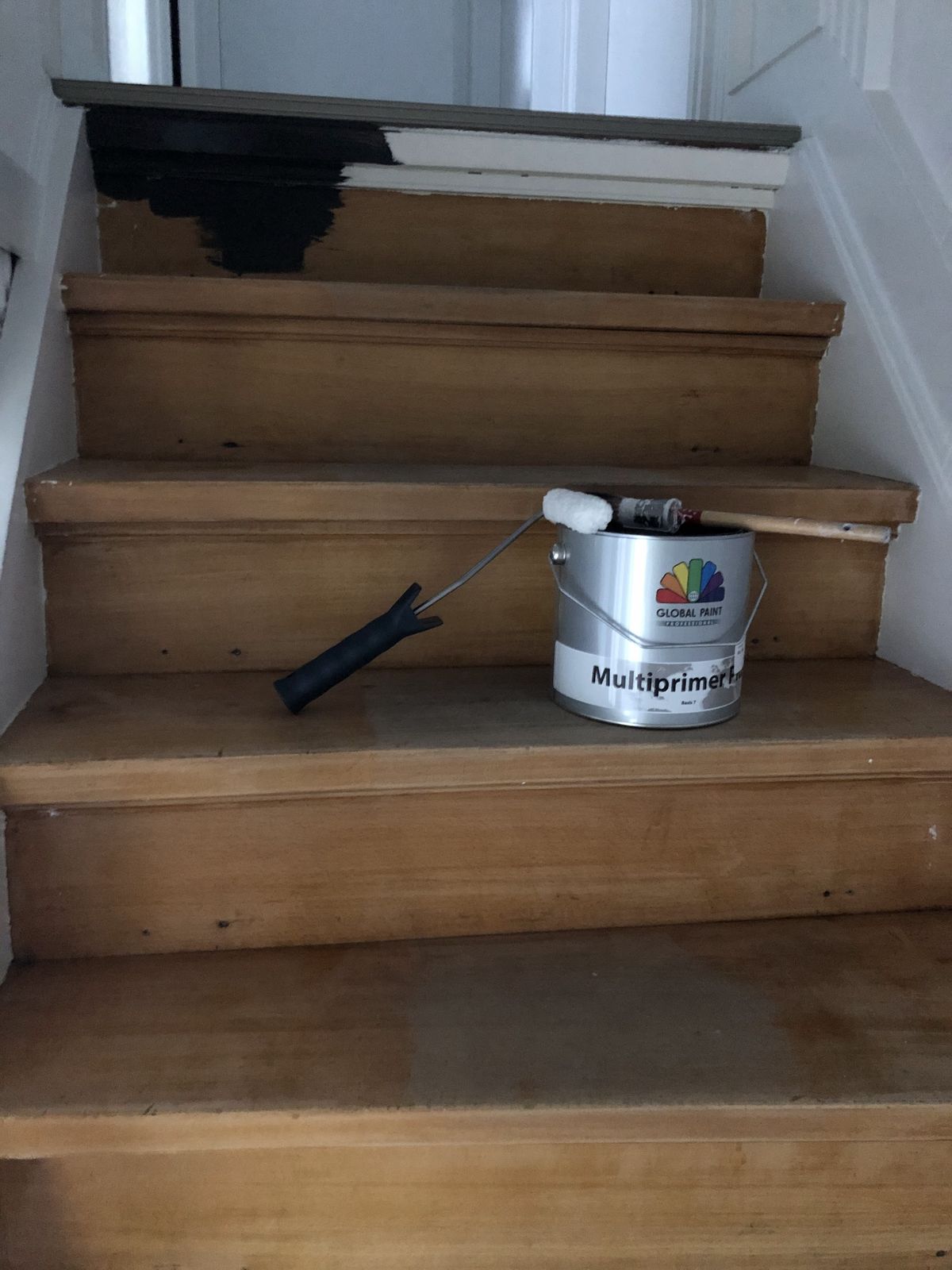 Houten trap in de voorbereiding, bovenste trede al voorgestreken, met een blik Multiprimer en een roller