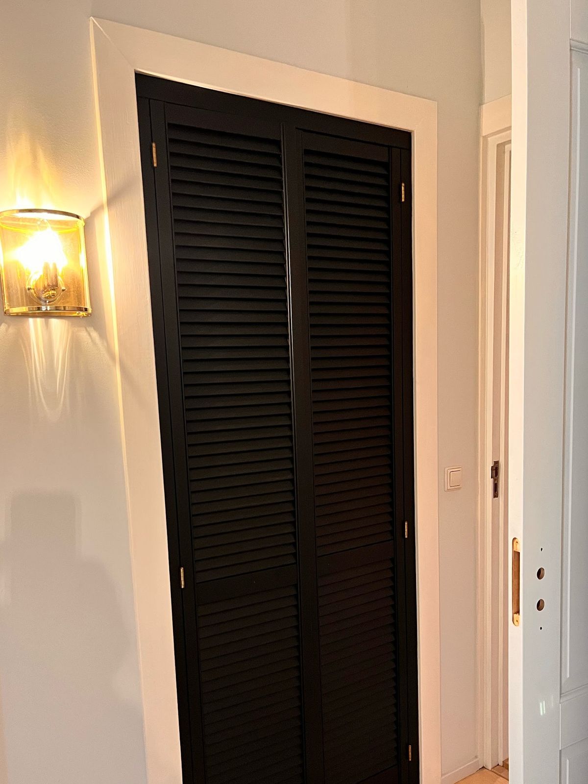 Binnendeur met lamellen diepzwart gelakt, witte kozijnen en een messing wandlamp