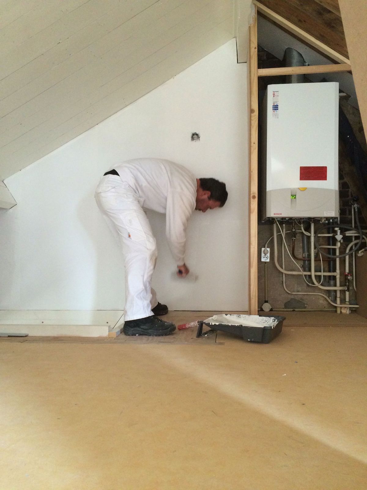 Schilder in witte werkkleding aan het werk aan een wand onder de trap