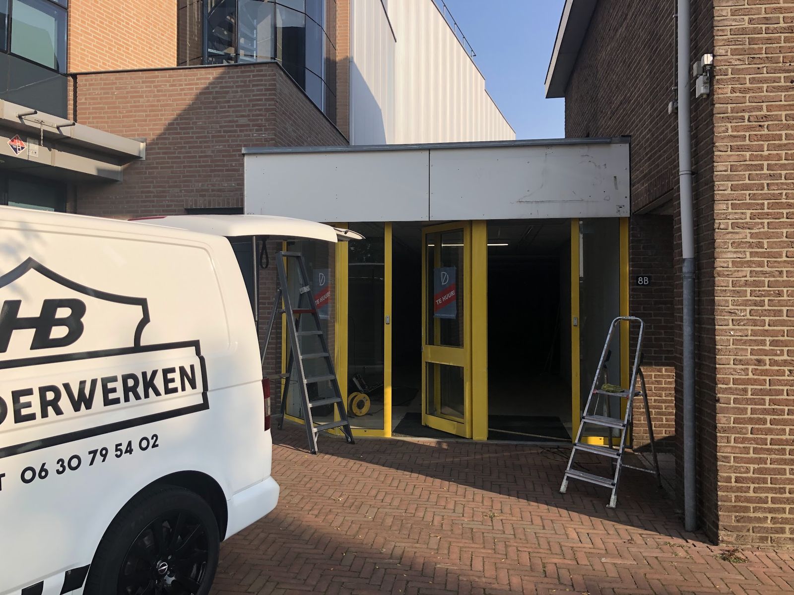 Witte bedrijfsbus van HB Schilderwerken bij een bedrijfspand met gele kozijnen en ladders